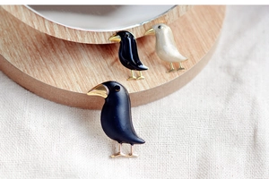 Detailed view of three bird-shaped enamel brooches in black and cream on a wooden base