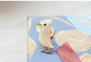 Macro detail of bird brooch showing shell texture and golden metal accents
