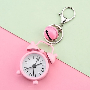 Detail view of a cute pink mini alarm clock keychain on a pastel background