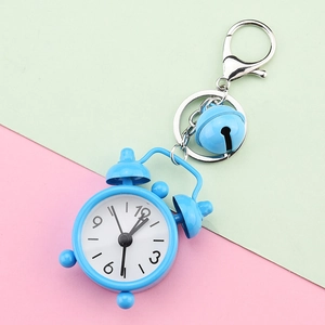 Close-up of a cute blue mini alarm clock keychain with a bell on pink and green background.