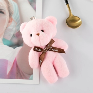 Detailed view of pink plush teddy bear keychain with Love ribbon on white surface