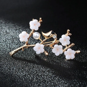 Detail of a gold bird and white flower brooch featuring a pearl and sparkling rhinestone