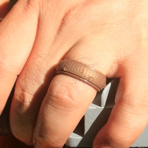 Detail of dark brown silicone ring with Greek pattern and water droplets on finger