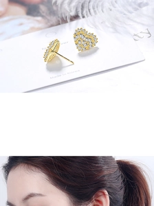 Detail view of heart-shaped gold earrings with sparkling white zircons on model's ear