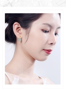 Detail of model wearing a gold clover-shaped earring with faceted sparkling zircon stones