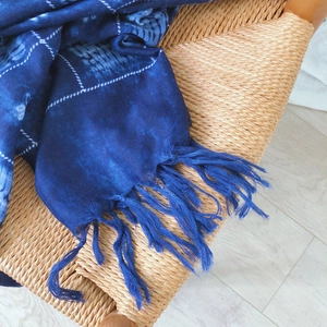 Blue tie-dye plaid cotton scarf with handmade tassels draped on a rattan chair