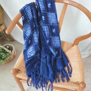 Detailed view of blue tie-dye plaid scarf with handmade tassels on a wooden chair