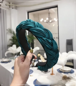 Detail of dark green pleated braided headband featuring glossy satin fabric texture