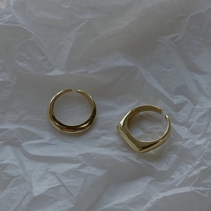 Detail view of gold-plated minimalist C-shaped open rings on white textured paper