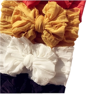 Close-up of baby headbands featuring large pleated bows in yellow, white, and black colors