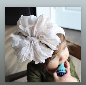 Close-up of a cream-colored baby headband with large layered pleated lace flower detail