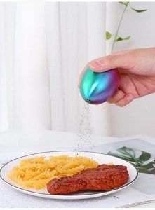Rainbow stainless steel egg-shaped shaker sprinkling spice over a fresh meal
