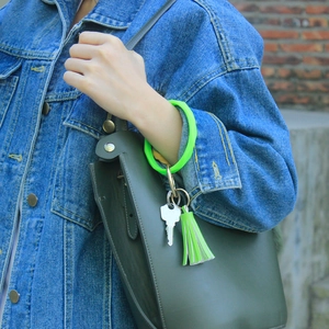 Neon green silicone wristband keychain with leather tassel shown on user wrist