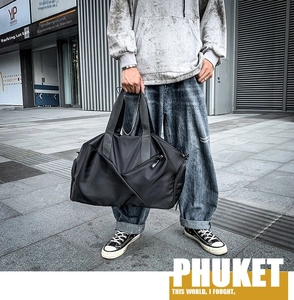 Close-up of a black waterproof travel bag with reinforced handles in a street setting