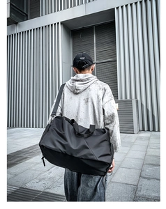 Rear view of a black waterproof sports travel bag worn by a model in a modern urban setting