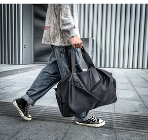 Close-up of black nylon travel bag with handles and side pockets held by a model