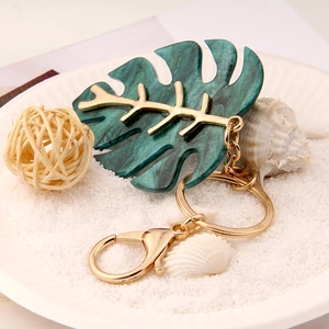 Tropical monstera leaf keychain with marble texture and gold veins on beach sand