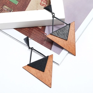 Détail de boucles d'oreilles triangulaires en bois brun et métal noir sur fond blanc neutre