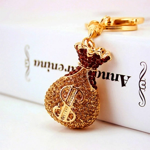 Golden money bag keychain with crystal rhinestones and dollar sign symbol on a white book