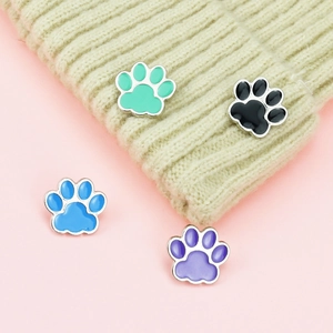 Detail of colorful paw print enamel pins on a beige knit hat and pink background