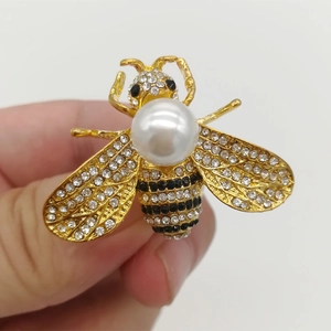 Macro view of gold bee brooch featuring sparkling rhinestones and a large faux pearl