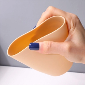 Flexible beige plastic toothbrush cup shown squeezed to demonstrate soft material