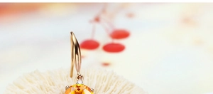 Detail of rose gold drop earring with orange round gemstone and small diamond accent