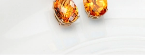 Close-up of gold stud earrings featuring faceted oval orange-yellow citrine gemstones