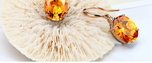 Detail of gold-plated drop earrings featuring large oval orange citrine gemstones and diamonds