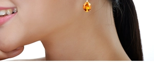 Close-up of an oval orange citrine earring set in a silver base on a model ear
