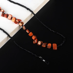 Detail of beaded sunglasses chain with orange shells and black beads on dual-tone background