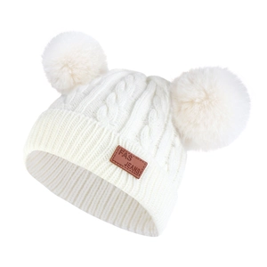 Detail of baby winter knit hat featuring double fur pom-poms and a leather brand patch