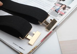 Close-up of black elastic belts featuring classic gold H-shaped metal buckles on a magazine