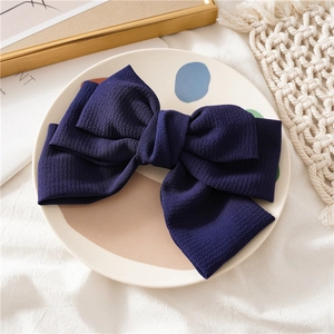Detail of a dark blue fabric triple-layered bow hair clip on a decorative background