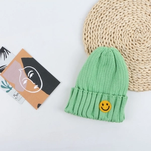 Detailed view of green knitted beanie featuring a yellow smiley face patch on the cuff