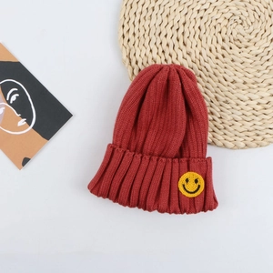 Detail of dark red ribbed knit beanie with a yellow smiley face patch for kids winter