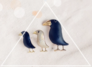 Detailed close-up of bird brooches in blue and cream enamel with gold plating on beige fabric