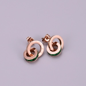 Close-up of rose gold interlocking earrings with Roman numerals and a green square gem
