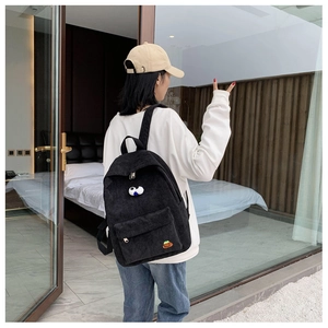 Close-up of black corduroy backpack with cute eye patches worn by a model in a bright room