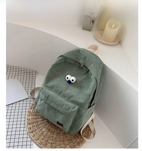 Detail of green corduroy backpack with cartoon eyes and small mountain patch decor