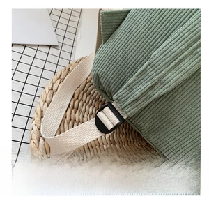 Detail showing adjustable cream-white webbing strap and green corduroy fabric of the backpack