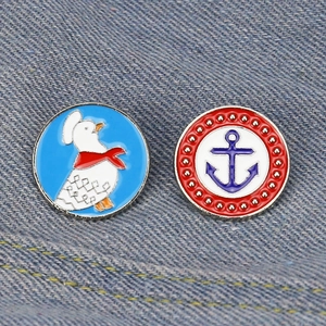 Set of two round metal enamel pins featuring a white duck and blue anchor on denim fabric