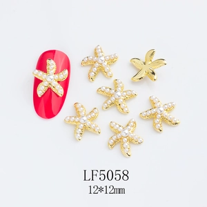 Macro detail of 12mm gold starfish nail charms with white pearls on red nail sample