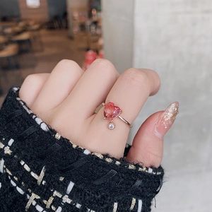 Detail of a rose gold heart ring with pink gemstone and dangling diamond on a model hand