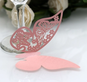 Macro shot of laser-cut pearl pink butterfly decorative seat card on a glass stem