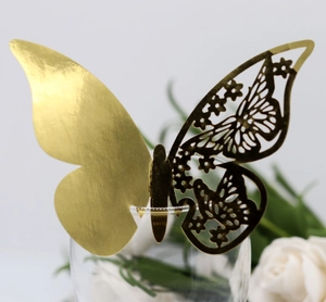 Macro shot of laser-cut hollow butterfly card in gold finish on a glass rim