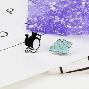 Detail shot of cute black cat enamel pin and blue origami mountain badge with glitter