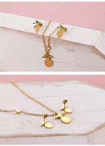 Macro view of gold pineapple jewelry set with green enamel leaves and clear gemstones