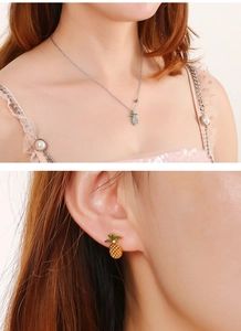 Close-up of cute silver pineapple necklace and gold earrings with green leaf details