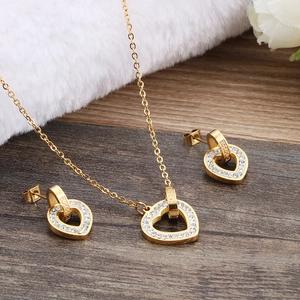 Elegant gold heart necklace and earrings set with crystals on a wooden background